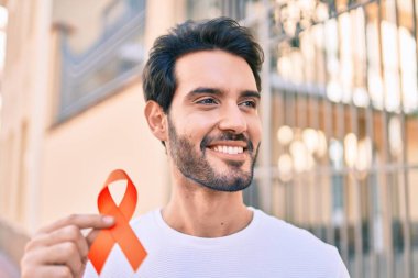 Genç İspanyol gülümseyen adam şehirde elinde turuncu kurdele tutarken mutlu..
