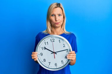 Güzel, orta yaşlı, sarışın bir kadın büyük saati tutuyor şüpheci ve gergin, sorun yüzünden kaşlarını çatıyor. negatif kişi. 