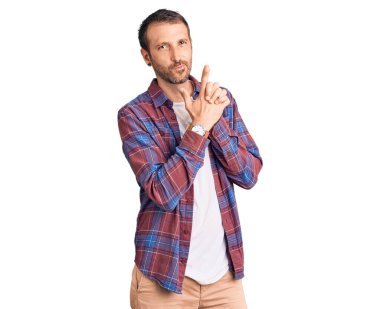 Genç yakışıklı bir adam gündelik giysiler içinde sembolik bir silah tutuyor. El hareketleriyle cinayet silahlarıyla oynuyor. Kızgın bir yüz. 