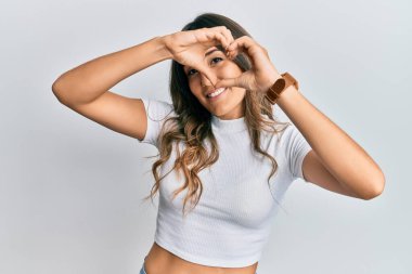 Genç esmer kadın, gündelik beyaz tişört giyiyor kalp şeklinde el ve parmakları ile tabelanın içinden bakıp gülümsüyor. 