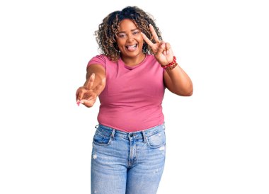 Genç Afro-Amerikan artı cüsseli kadın günlük kıyafetler giyiyor, dili dışarı fırlamış bir şekilde gülümsüyor ve iki elini de zafer işareti yapıyor. İki numara.. 