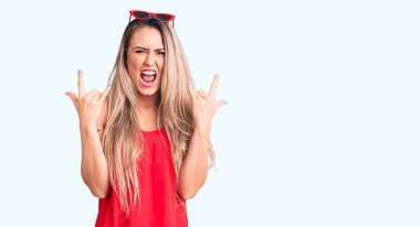 Kolsuz tişört giyen, güneş gözlüklü, çılgın bir ifadeyle bağıran, elleri havada rock sembolü yapan genç, güzel sarışın kadın. Müzik yıldızı. ağır kavram. 