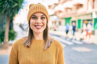 Kış tarzı giyinen genç sarışın kadın şehirde mutlu bir şekilde gülümsüyor..