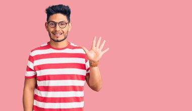 Yakışıklı Latin Amerikalı gündelik kıyafetler ve gözlük takan genç adam beş numarayı gösterip işaret ederken kendinden emin ve mutlu gülümsüyor.. 