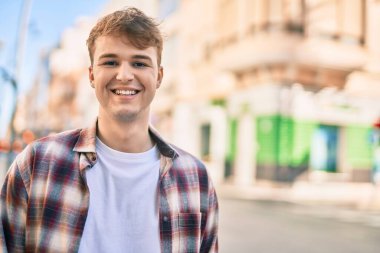 Genç beyaz adam gülümseyerek şehirde mutlu mesut duruyor..