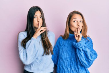 Tüylü, kışlık kazak giyen anne ve kızın İspanyol ailesi parmakları dudaklarında sessiz olmak istiyorlar. sessizlik ve gizli konsept. 