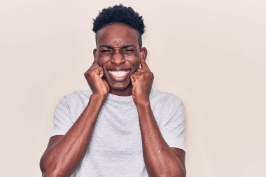 Genç Afro-Amerikan adam gündelik kıyafetler giyip yüksek sesli müzik sesi için kulaklarını parmaklarıyla kapatıyor. sağır kavramı. 