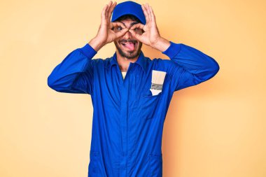 Kıvırcık saçlı ve ayı kılıklı yakışıklı bir adam. İnşaatçı tulumu giyiyor. Dürbün gibi jest yapıyor. çılgın ifade. 