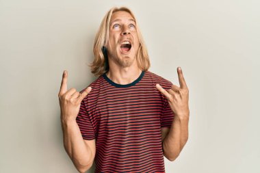 Caucasian young man with long hair doing rock gesture angry and mad screaming frustrated and furious, shouting with anger looking up. 