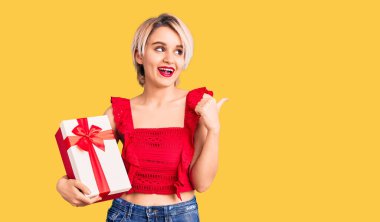 Sarışın, güzel bir kadın elinde hediyeyle baş parmağını kaldırmış, ağzı açık gülümsüyor. 