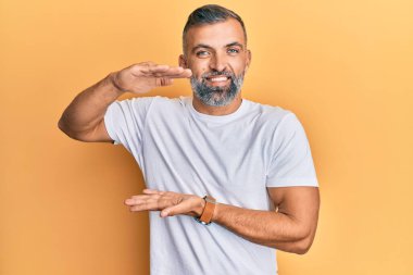 Orta yaşlı, beyaz tişört giyen, elleri büyük ve büyük bir işaret gösteren orta yaşlı, yakışıklı bir adam. Kameraya bakıp gülümsüyor. ölçüm kavramı. 