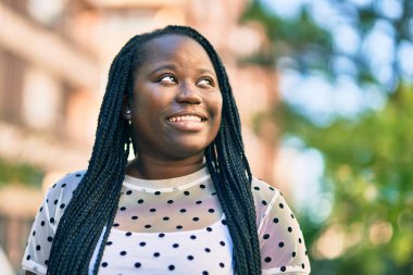 Genç Afrikalı Amerikalı kadın gülümseyerek şehirde mutlu mesut duruyor..