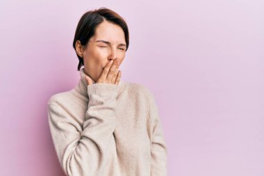 Kısa saçlı, kış süveteri giyen genç esmer kadın ağzıyla esnemekten sıkılmış. Huzursuz ve uykulu.. 