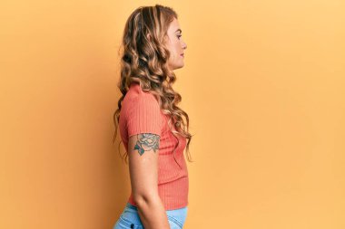 Sıradan kıyafetler giyen genç sarışın kız rahat bir görünüm takınıyor kendine güvenen bir gülümsemeyle doğal bir yüz ifadesi takınıyor.. 