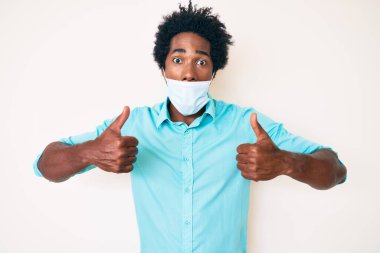 Yakışıklı, Afro saçlı, tıbbi maske takan, komik bir ifadeyle dilini dışarı çıkaran Afro-Amerikan bir adam.. 