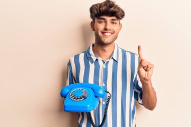 Elinde klasik bir telefonla gülümseyen genç İspanyol bir adam bir fikir veya soru işareti ile mutlu bir yüzle, bir numara 