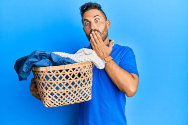 Sakallı yakışıklı bir adam çamaşır sepetini tutarken ağzını eliyle kapatıyor, şok geçiriyor ve hata yapmaktan korkuyor. şaşırmış ifade 