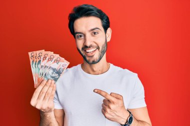 Avustralya doları tutan genç İspanyol adam mutlu bir şekilde elini ve parmağını gösterdi. 