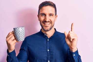 Young handsome businessman drinking mug of coffee over isolated pink background smiling happy pointing with hand and finger to the side