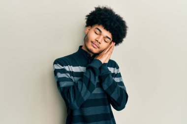 Afro saçlı, sıradan kıyafetler giyen, yorgun uyuyan, hayal kuran ve elleri ve elleri kapalı gülümserken poz veren Afro-Amerikan genç adam.. 