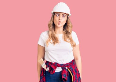 Güvenlik kaskı takan genç beyaz kadın dudaklarıyla balık suratı yapıyor, çılgınca ve komik bir jest. Komik ifade. 