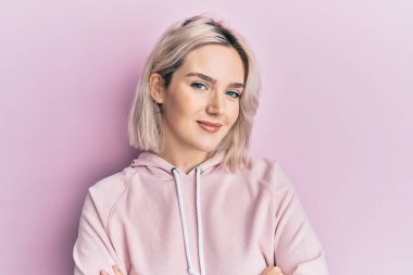 Sıradan kıyafetler giyen, kollarını kavuşturup kameraya bakan mutlu yüzlü genç sarışın kız. pozitif kişi. 