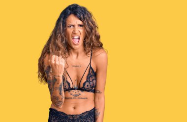 Dövmeli genç İspanyol kadın. İç çamaşırı giyiyor. Kızgın ve kızgın. Öfkeyle bağırırken yumruk kaldırıyor. öfke ve agresif konsept. 