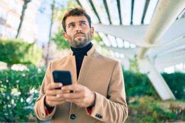 Zarif ceketli yakışıklı bir iş adamı. Açık havada akıllı telefon kullanıyor.