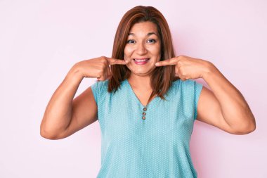 Orta yaşlı esmer, sıradan kıyafetler giyen neşeli gülümseyen ve parmaklarıyla ve ağzıyla işaret eden İspanyol kadın. diş sağlığı kavramı. 
