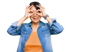 Kısa saçlı, sıradan bir kot ceket giyen, dilini dışarı çıkaran dürbün gibi jest yapan, parmaklarından bakan güzel İspanyol bir kadın. çılgın ifade. 