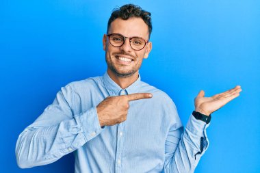 Gündelik kıyafetler giyen ve gözlüklü genç İspanyol adam kameraya hayret ediyor ve gülümsüyor.. 