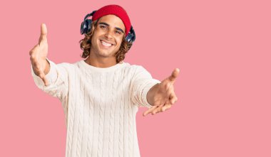 Genç İspanyol adam müzik dinliyor kulaklık takıyor kameraya bakıyor sarılmak için kollarını açmış gülümsüyor. Mutluluğu kucaklayan neşeli bir ifade.. 