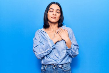 Gündelik kıyafetler giyen, göğsünde elleri kapalı, yüzünde minnet dolu bir jest olan genç ve güzel bir Latin kadın. sağlık kavramı. 