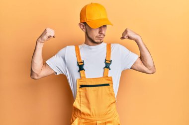 Tamirci üniforması giyen İspanyol genç adam gururla gülümseyen kol kaslarını gösteriyor. fitness konsepti. 