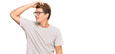 Yakışıklı beyaz adam, günlük kıyafetler ve gözlük takıyor, gülümsüyor, saçlarına dokunuyor, el hareketi yapıyor, çekici ve modaya uygun poz veriyor. 