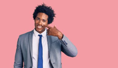 Afro saçlı, iş ceketi giyen, el parmakları ve burunlarıyla gülümseyen yakışıklı Afro-Amerikan bir adam. güzellik konsepti 