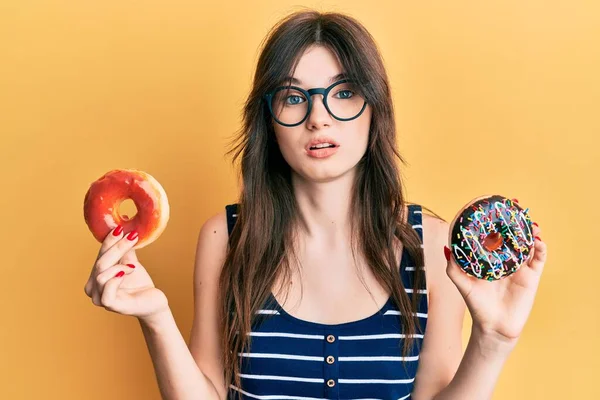 年轻美丽的高加索女孩 手里拿着美味的五颜六色的甜甜圈 毫无头绪 面目全非 怀疑概念 — 图库照片