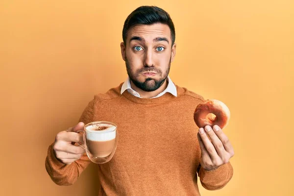 Young Hispanic Man Eating Doughnut Drinking Coffee Puffing Cheeks Funny — Stock Photo, Image