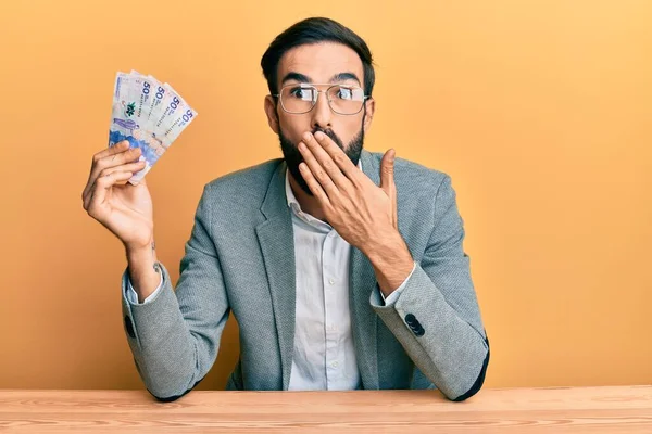 Jovem Hispânico Segurando Notas Pesos Colombianos Sentados Mesa Cobrindo Boca — Fotografia de Stock