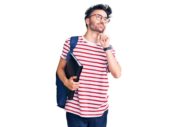 若いヒスパニック系の男を着て学生のバックパックと眼鏡を保持バインダー深刻な顔を考えて質問について手であご 混乱のアイデアについて思慮深い — ストック写真