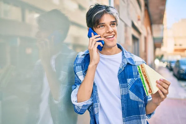 Fiatal Spanyol Férfi Mosolyog Boldog Beszél Okostelefonon Eszik Szendvicset Városban — Stock Fotó