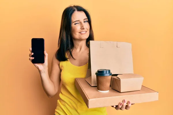 Middle Age Brunette Woman Holding Take Away Food Showing Smartphone — Φωτογραφία Αρχείου