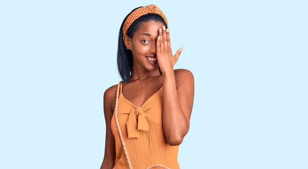 年轻的非洲裔美国女人穿着夏装 一只手捂住眼睛 脸上挂着自信的微笑 还有令人惊讶的情绪 — 图库照片