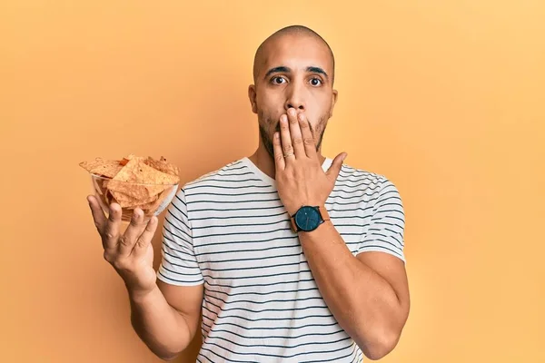 Hispanic Adult Man Holding Nachos Potato Chips Covering Mouth Hand — Stockfoto