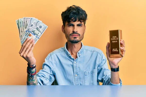 Young Hispanic Man Holding Dollars Gold Ingot Skeptic Nervous Frowning — Stock Photo, Image