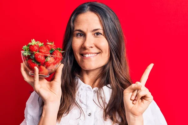 Joven Hermosa Morena Sosteniendo Tazón Fresas Saladas Sobre Fondo Rojo —  Fotos de Stock