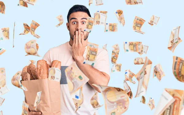 Genç, yakışıklı bir adam elinde ekmek torbasıyla ağzını eliyle kapatıyor, şokta ve hata yapmaktan korkuyor. şaşırmış ifade