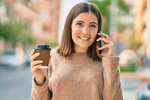 若いヒスパニック系の女性が街のスマートフォンのコーヒーを飲む話 — ストック写真