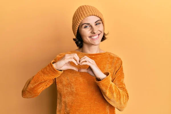 ウールの帽子と冬のセーターを身に着けている若いブルネットの女性は 心のシンボルと手で形を示す愛に微笑む ロマンチックなコンセプト — ストック写真