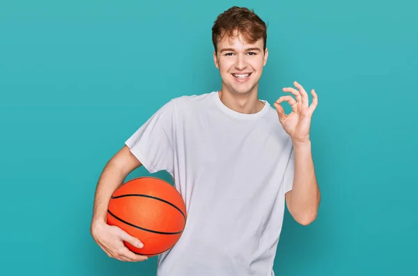 Pemuda Kaukasia Memegang Bola Basket Melakukan Tanda Dengan Jari Tersenyum — Stok Foto